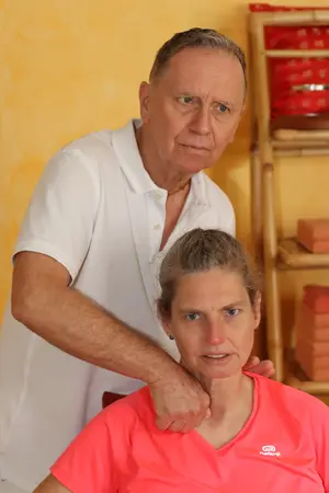 Ein älterer Mann führt eine Nackenmassage bei einer Frau in entspannter Praxisumgebung durch.
