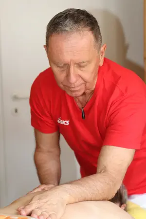 Ein älterer Mann in rotem Shirt führt eine therapeutische Rückenmassage durch.